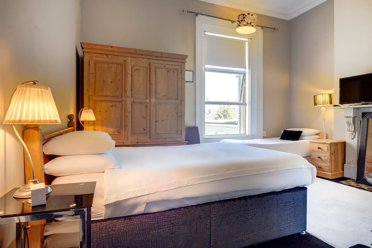 A bedroom with a large bed, a wooden wardrobe, a television, and a fireplace.