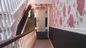 Un escalier avec une rampe blanche, une porte en bas et un papier peint à motifs floraux sur les murs.