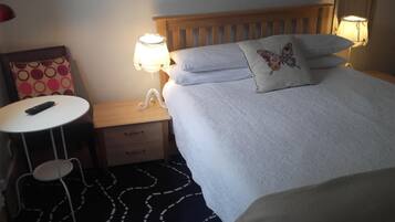 Habitación de hotel con una cama, lámparas de noche, una mesita con un control remoto, una silla y una alfombra estampada.