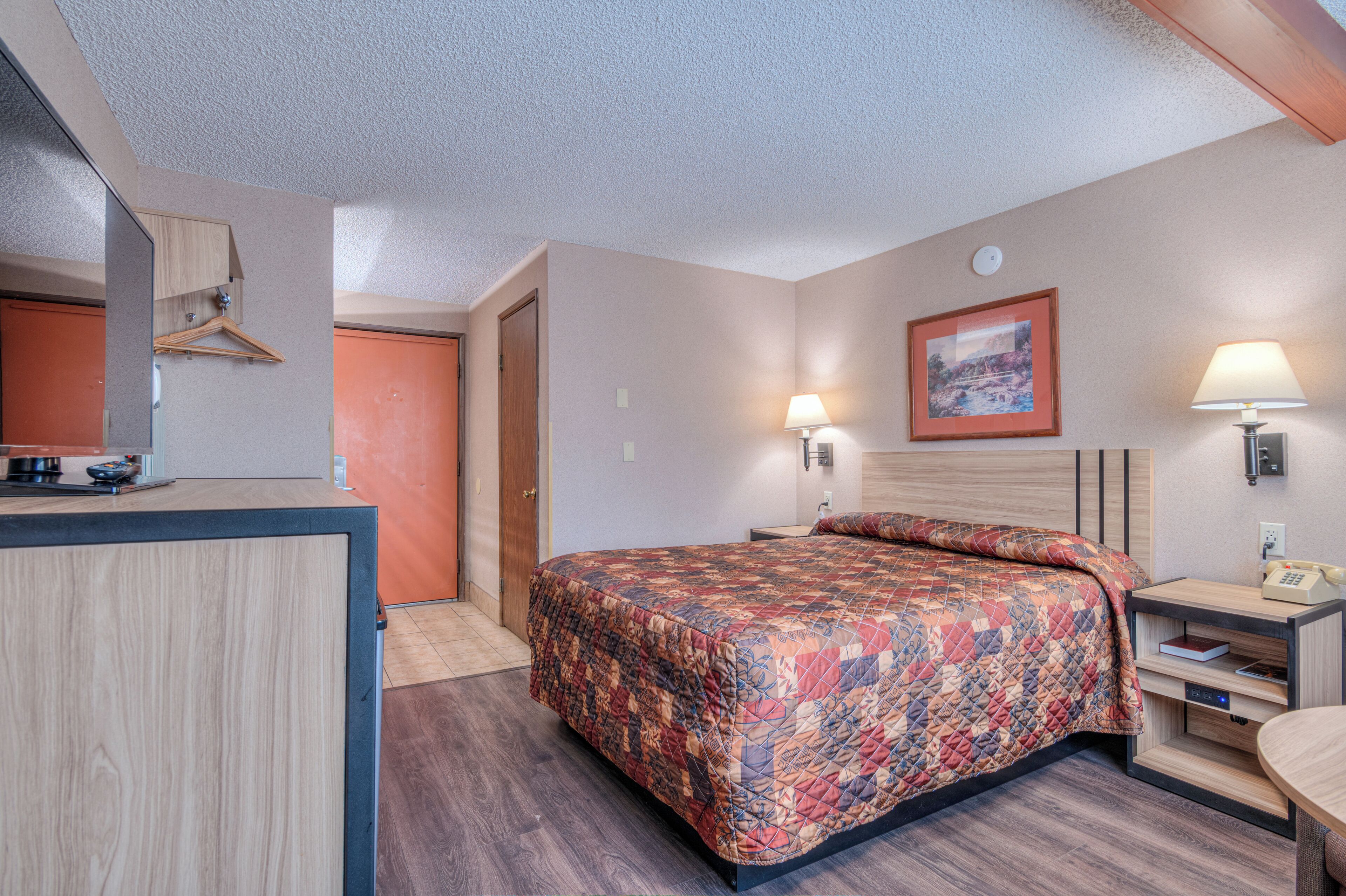 Habitación de hotel con cama, mesita de noche, lámpara y escritorio con teléfono.