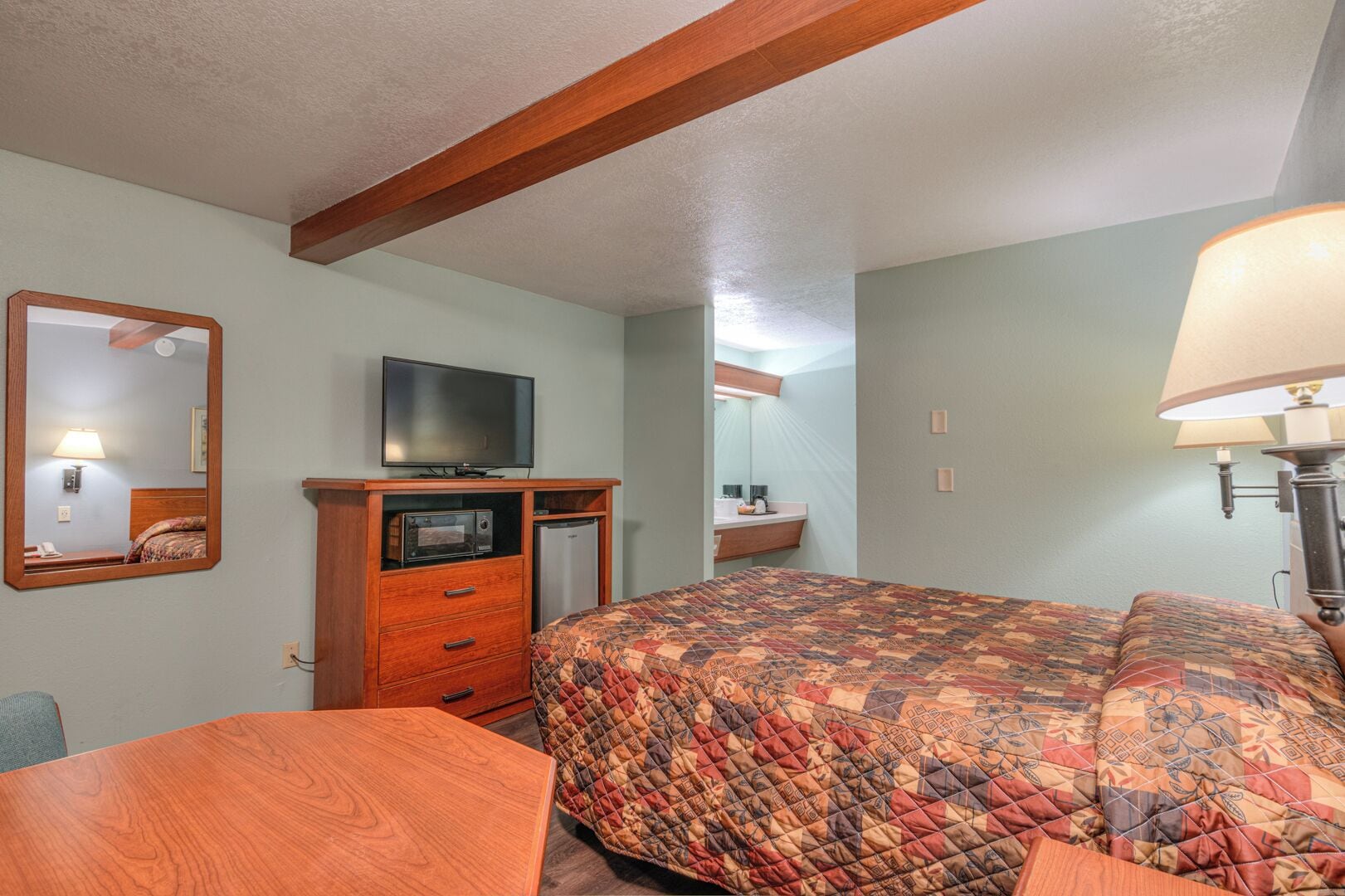 A hotel room with a bed, a television, a wooden dresser, and a desk.