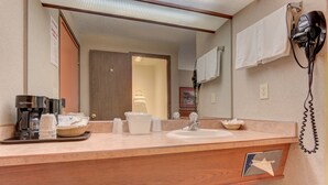 A hotel bathroom with a wooden vanity, a sink, a hairdryer, and a coffee maker.