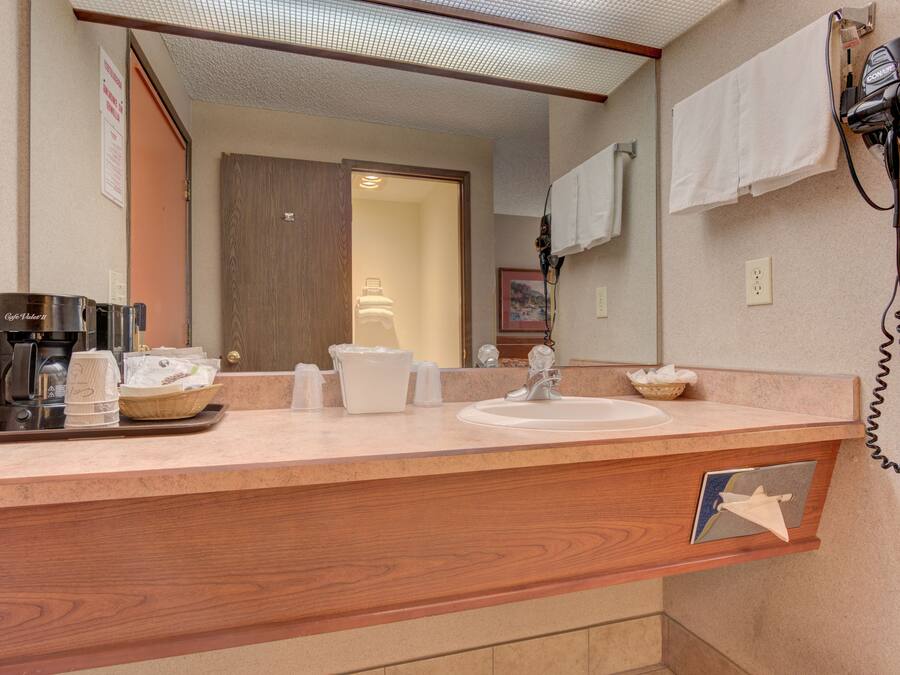 Une salle de bain d’hôtel équipée d’un meuble-lavabo en bois, d’un évier, d’un sèche-cheveux et d’une machine à café.