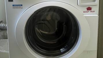 Una lavadora de carga frontal con pantalla digital, identificada como 'WASHER - LAVADORA', y un dispensador de detergente.
