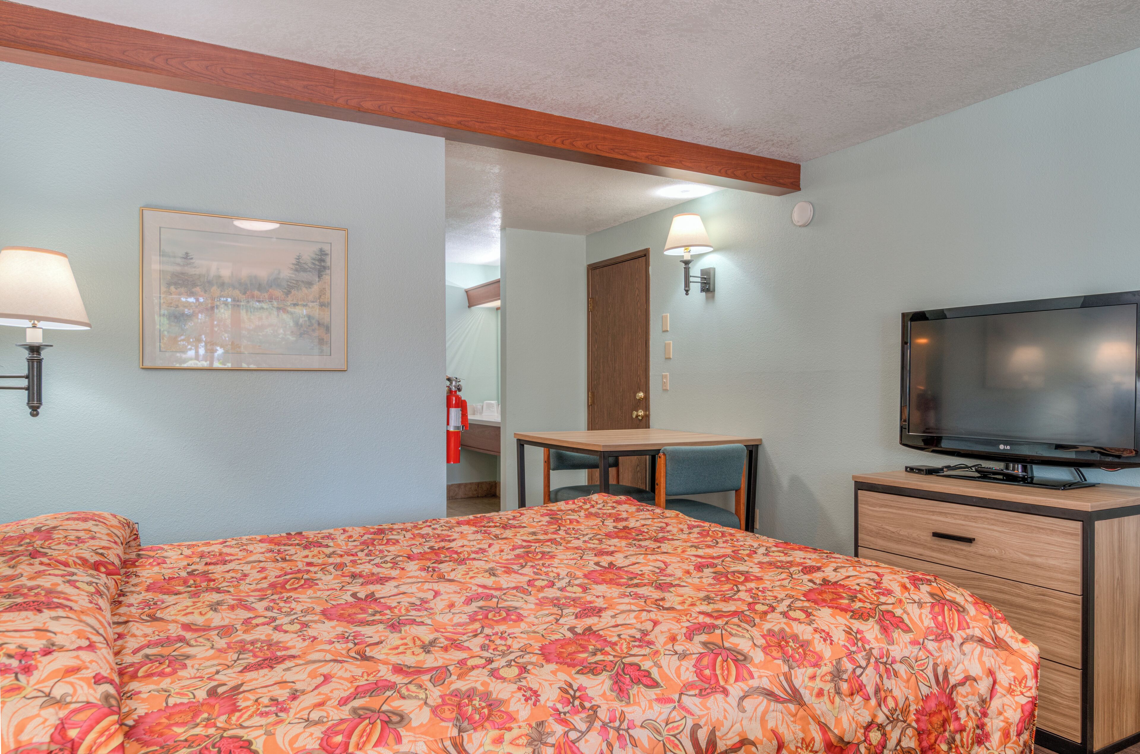 A hotel room with a bed, a desk, a television, and a fire extinguisher.