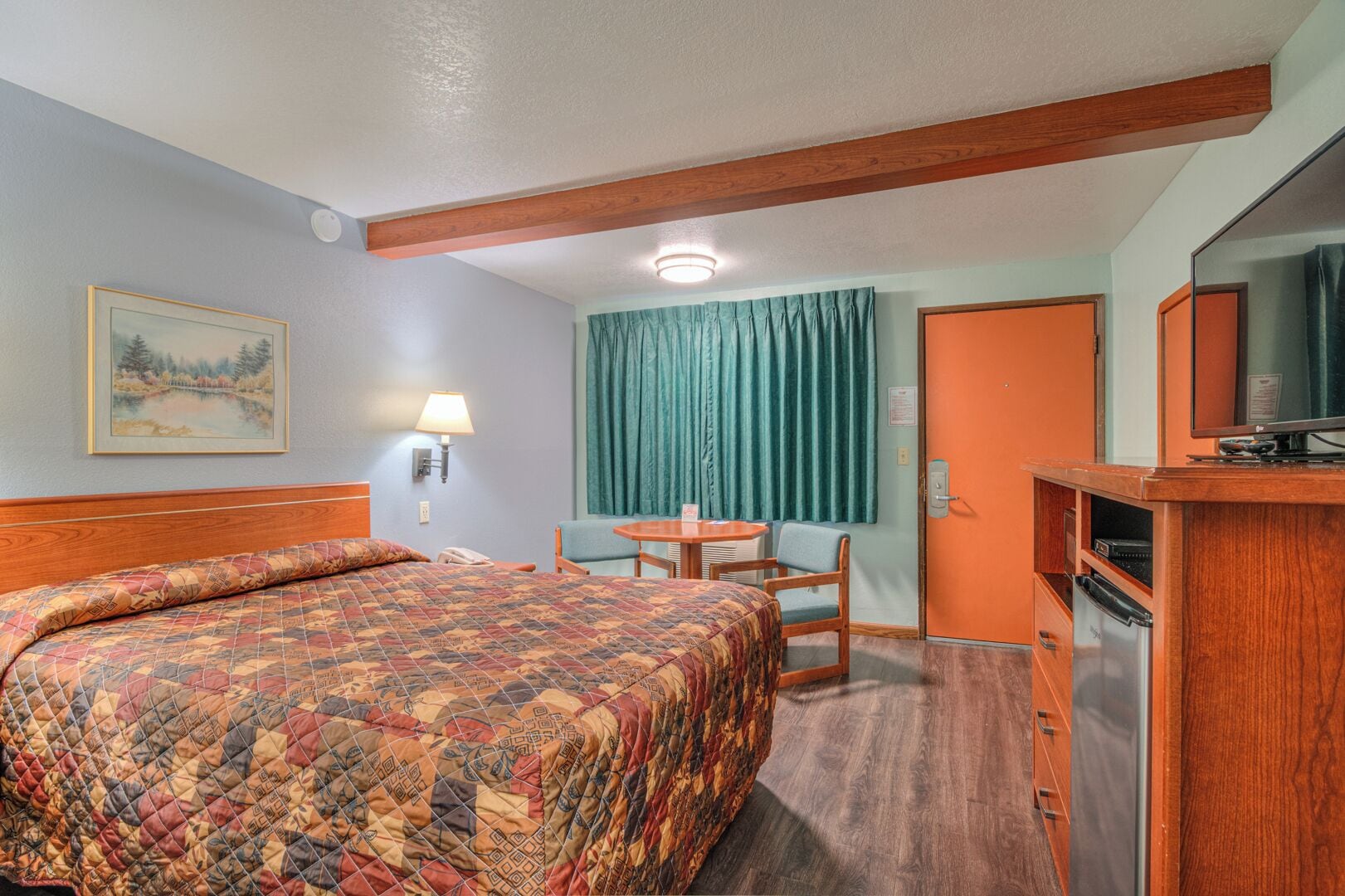 A hotel room with a bed, a desk, a chair, a television, and a refrigerator.