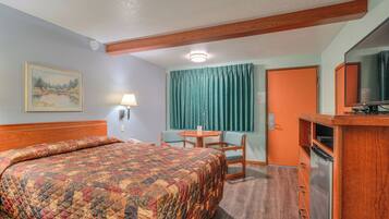 A hotel room with a bed, a desk, a chair, a television, and a refrigerator.