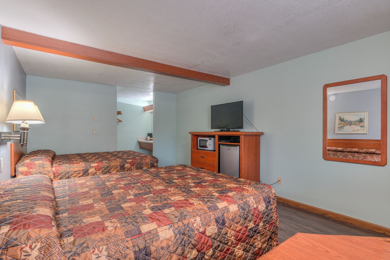 A room with two beds, a television, a microwave, and a refrigerator.