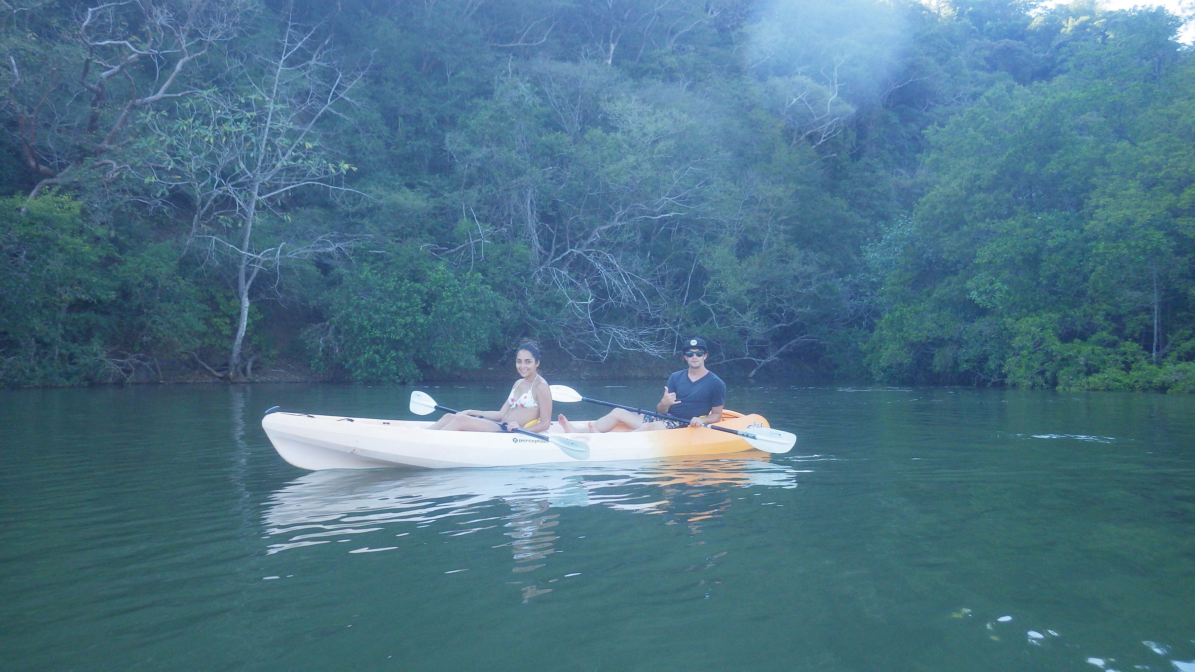 A couple in a kayak on a calm river surrounded by dense greenery.