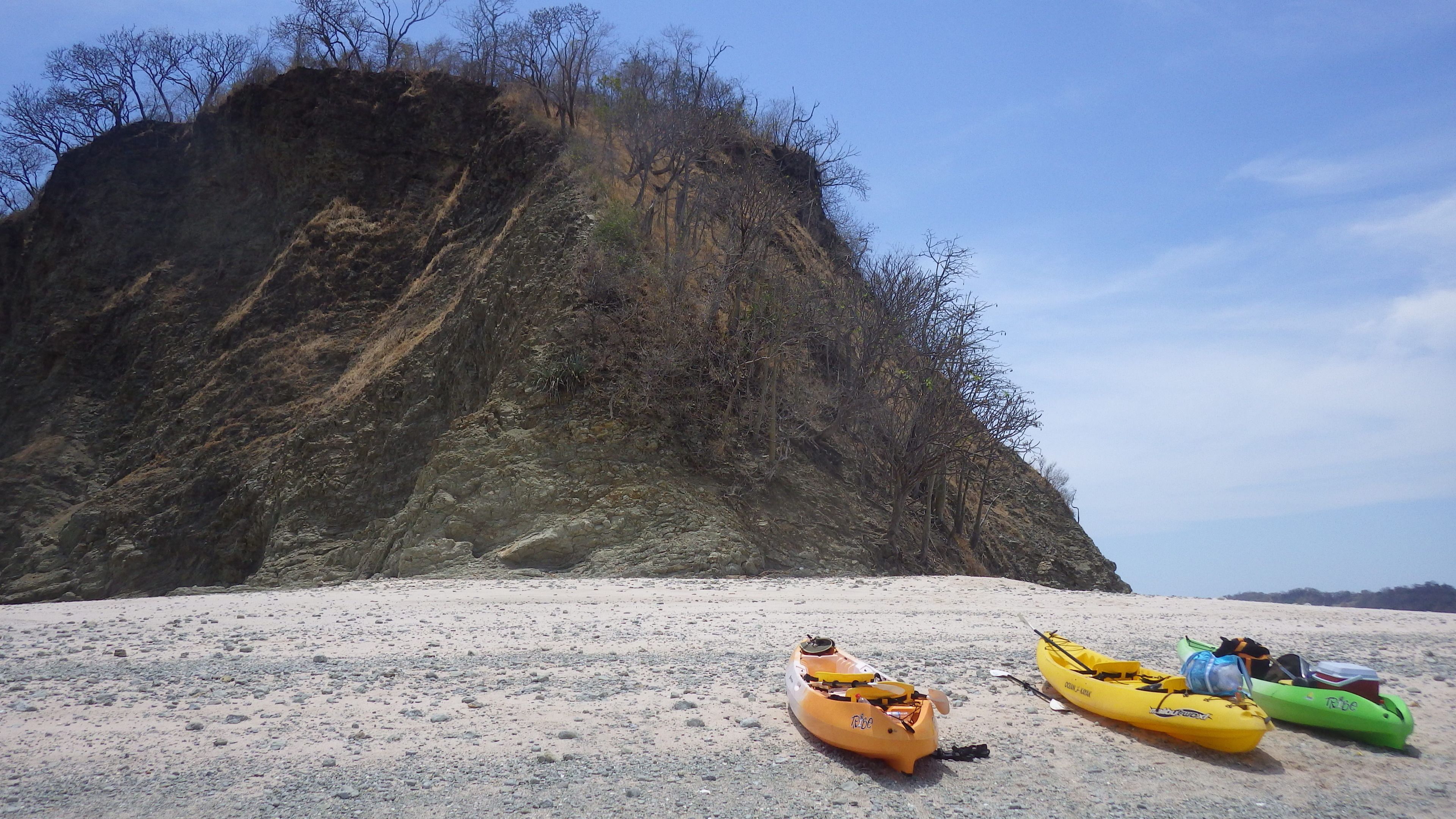 Kayaks on a sandy beach with a rocky cliff in the background.