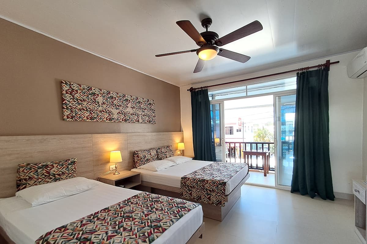Habitación de hotel con dos camas, un ventilador de techo, un papel tapiz estampado y vistas al exterior.