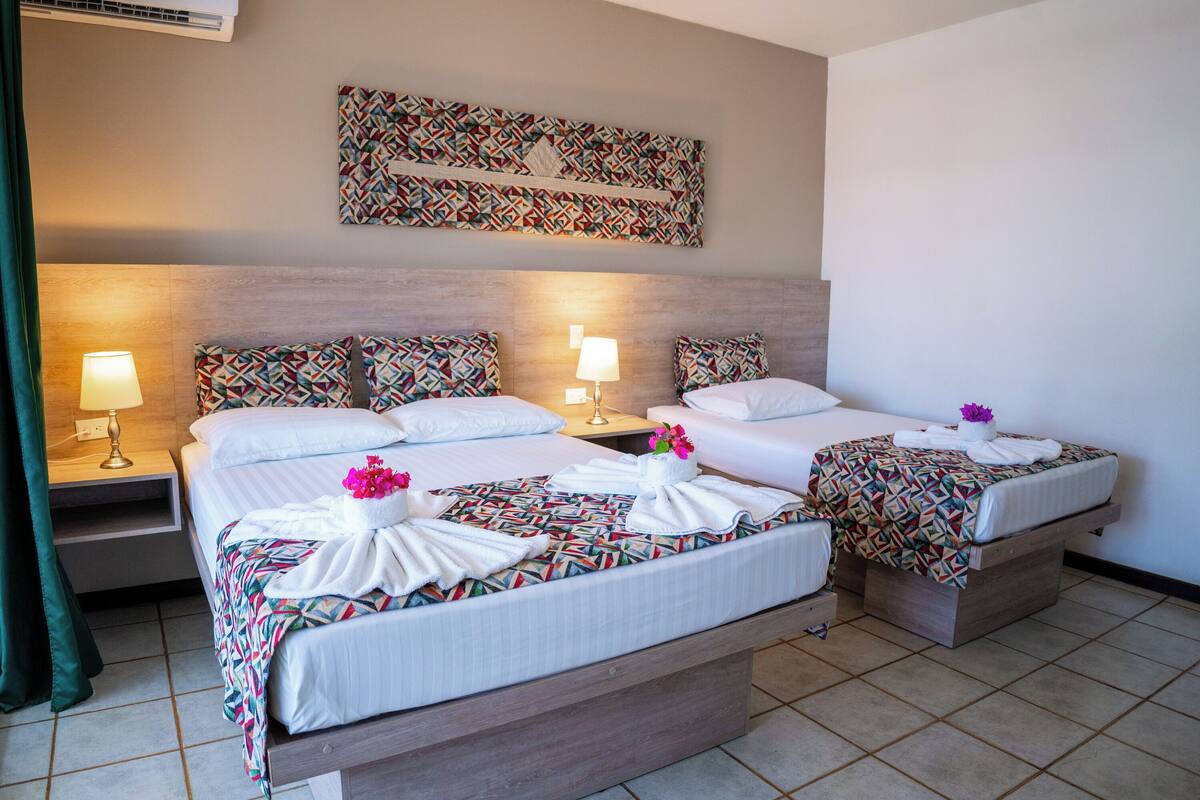 Habitación de hotel con dos camas, cada una con colcha y almohadas estampadas, cabeceros, lámparas de noche y un elemento decorativo en la pared sobre las camas.