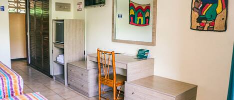 Una habitación de hotel con cama, escritorio, silla, armario y espejo.