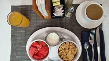 A breakfast tray with milk, cereal, and watermelon slices, a cup of coffee, and a glass of orange juice on a table.