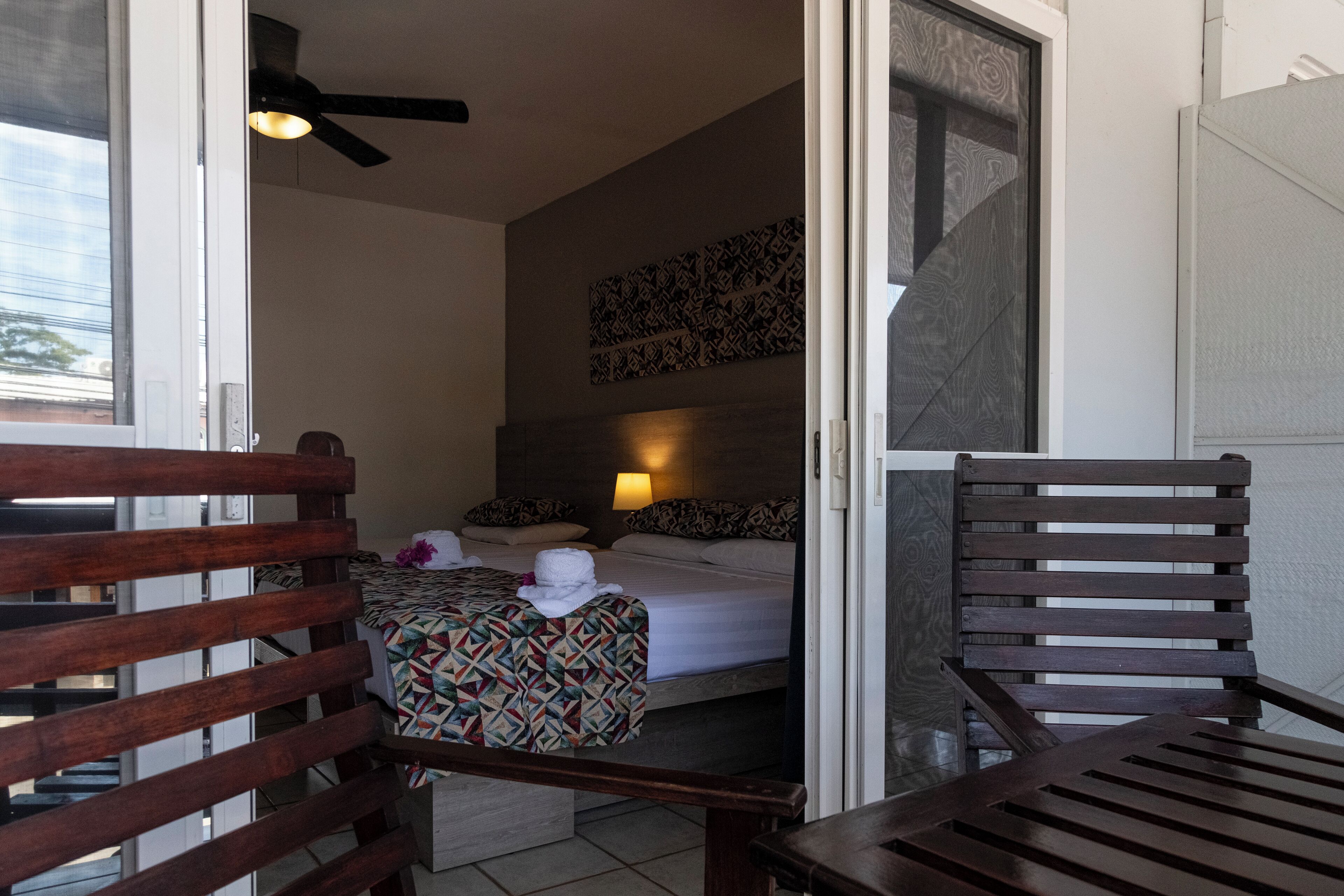 A hotel room with a bed, a chair, a ceiling fan, and a wall-mounted light.