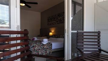 A hotel room with a bed, a chair, a ceiling fan, and a wall-mounted light.