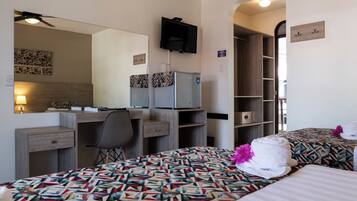A hotel room with a desk, two beds, a wardrobe, a mirror, and a television.