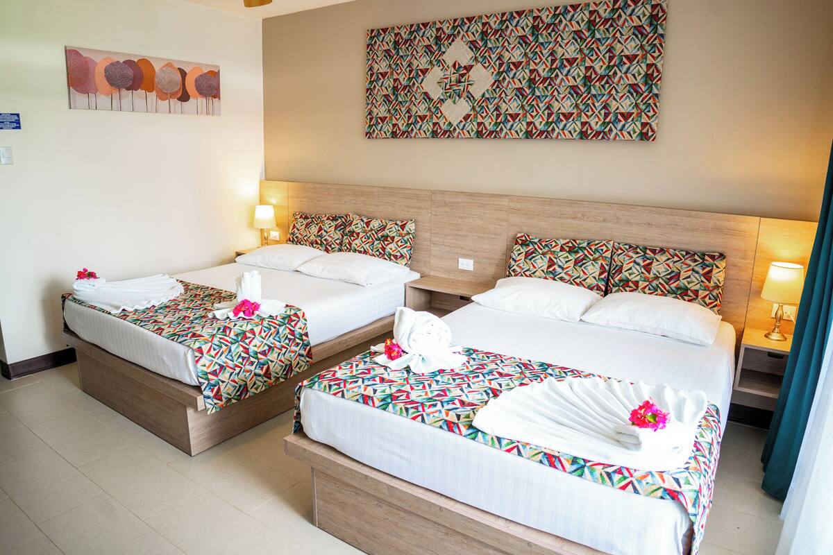 Habitación de hotel con dos camas, cada una con colcha y almohadas estampadas, cabeceros de madera y una pared decorada con una obra de arte de diseño geométrico.