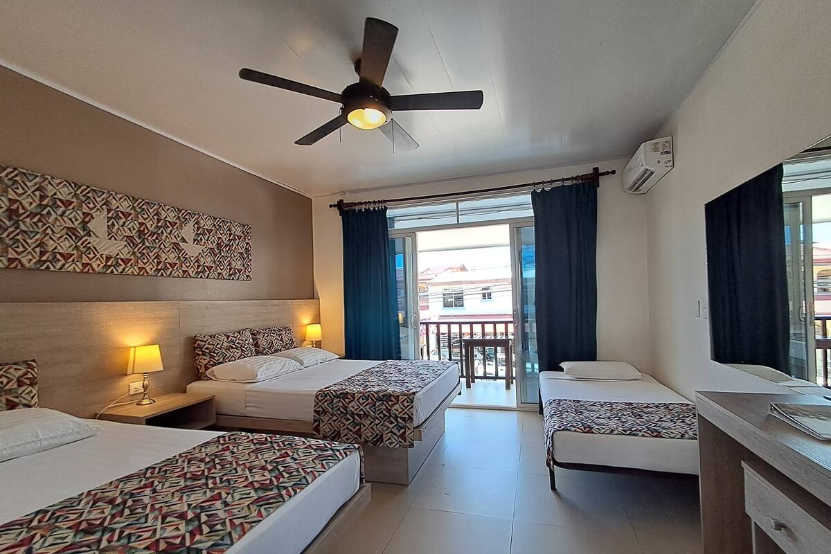 Habitación de hotel con dos camas, ventilador de techo, balcón con vistas y pared con diseño.
