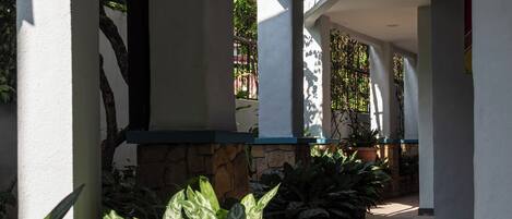 A covered corridor with tiled flooring, potted plants, and white pillars.