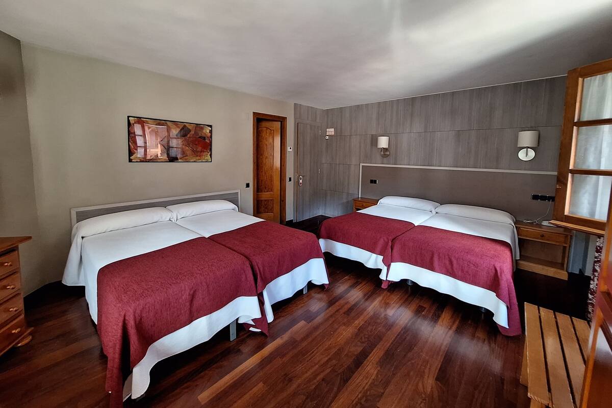 Habitación de hotel con dos camas, suelo de madera, un cuadro en la pared y una mesita de noche con una lámpara.