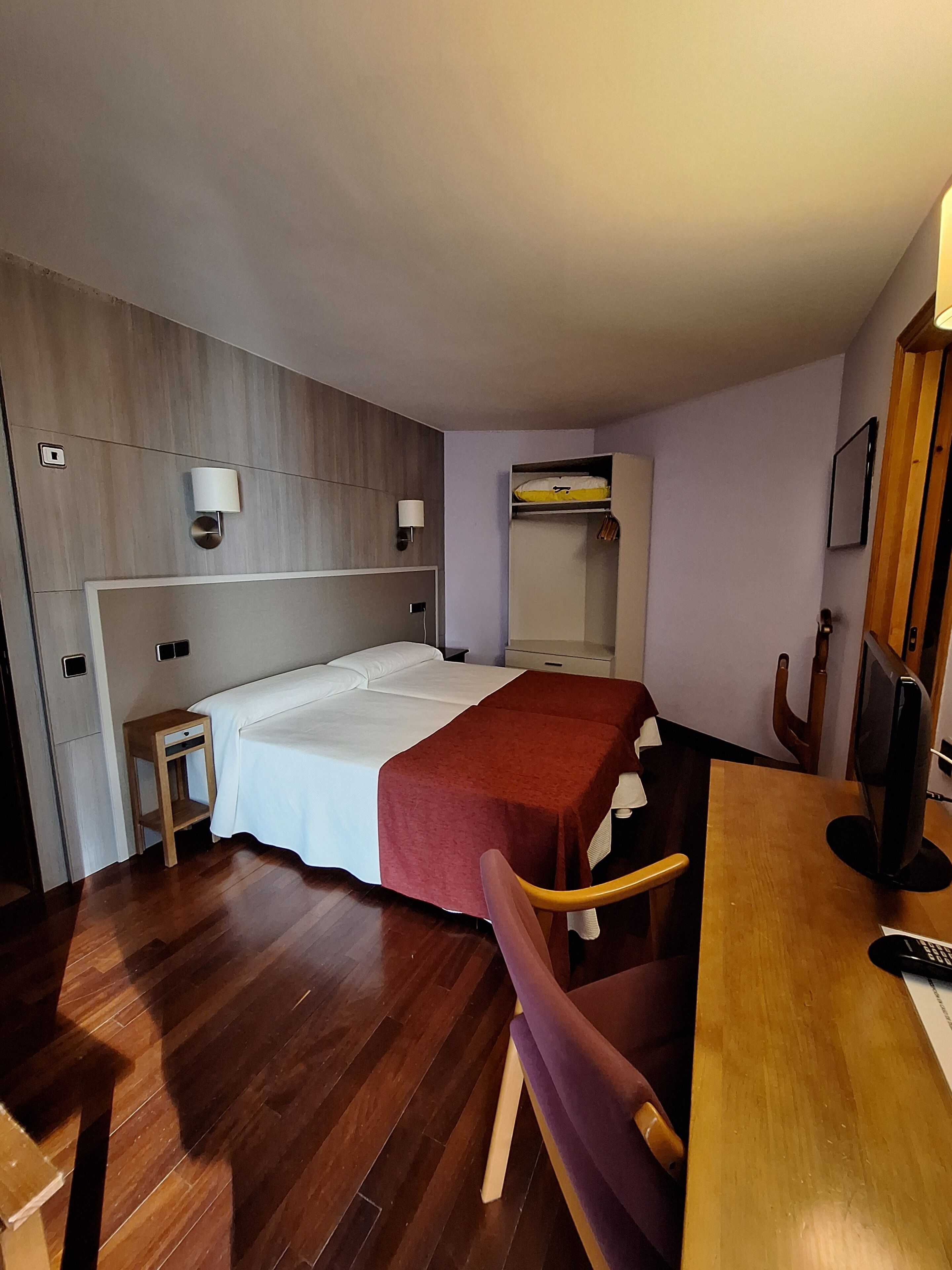 Une chambre d’hôtel comprenant un lit, une table de chevet, une chaise, un bureau, une télévision et une armoire.