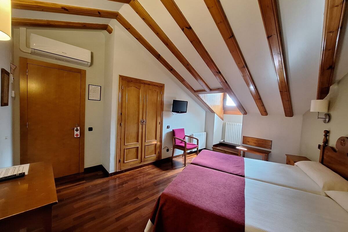 Una habitación con vigas de madera, una cama, un escritorio, una silla y un televisor.