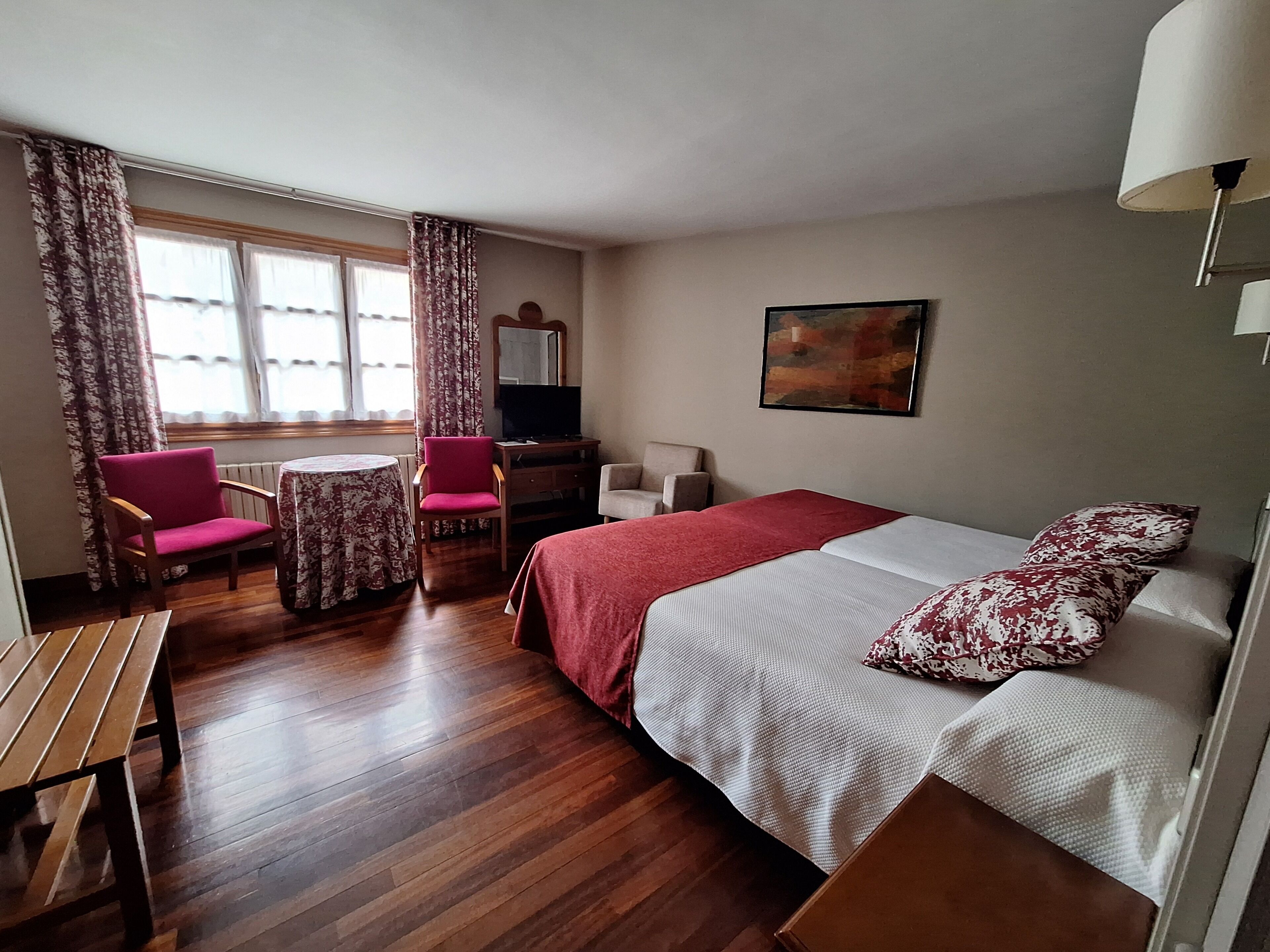Una habitació d'hotel amb un llit, un escriptori, una cadira, una taula petita i una televisió.