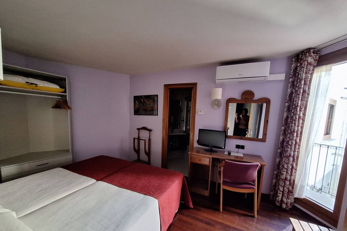 Habitación de hotel con cama, escritorio, silla y ventana con cortinas.
