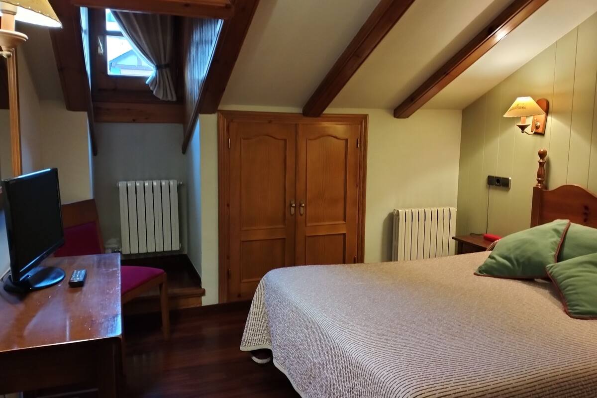 Un dormitorio con cama, escritorio con computadora, silla, armario de madera y ventana con cortinas.