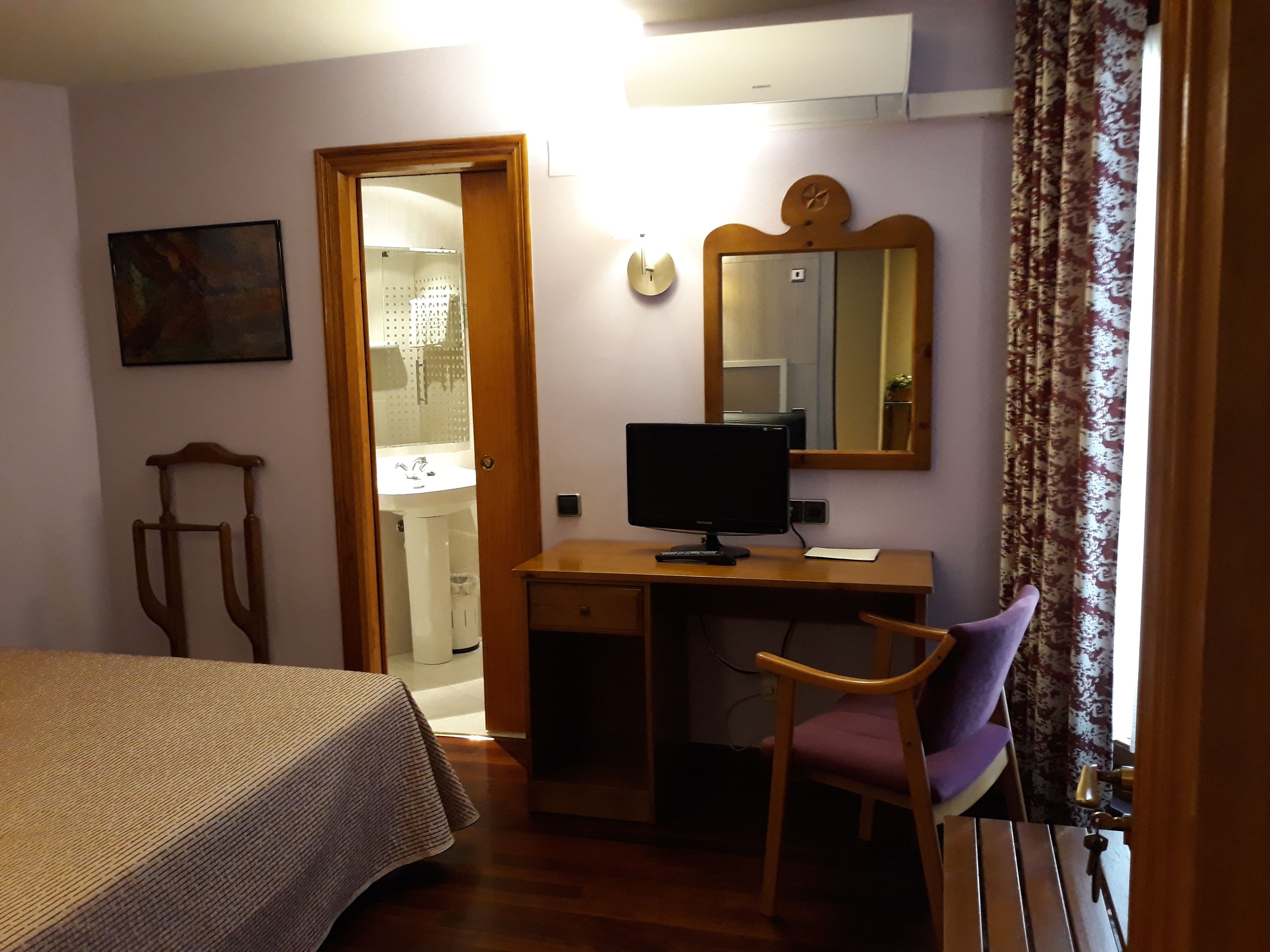 Una camera da letto con un letto, una scrivania con un computer, una sedia, uno specchio e una porta che dà su un bagno.