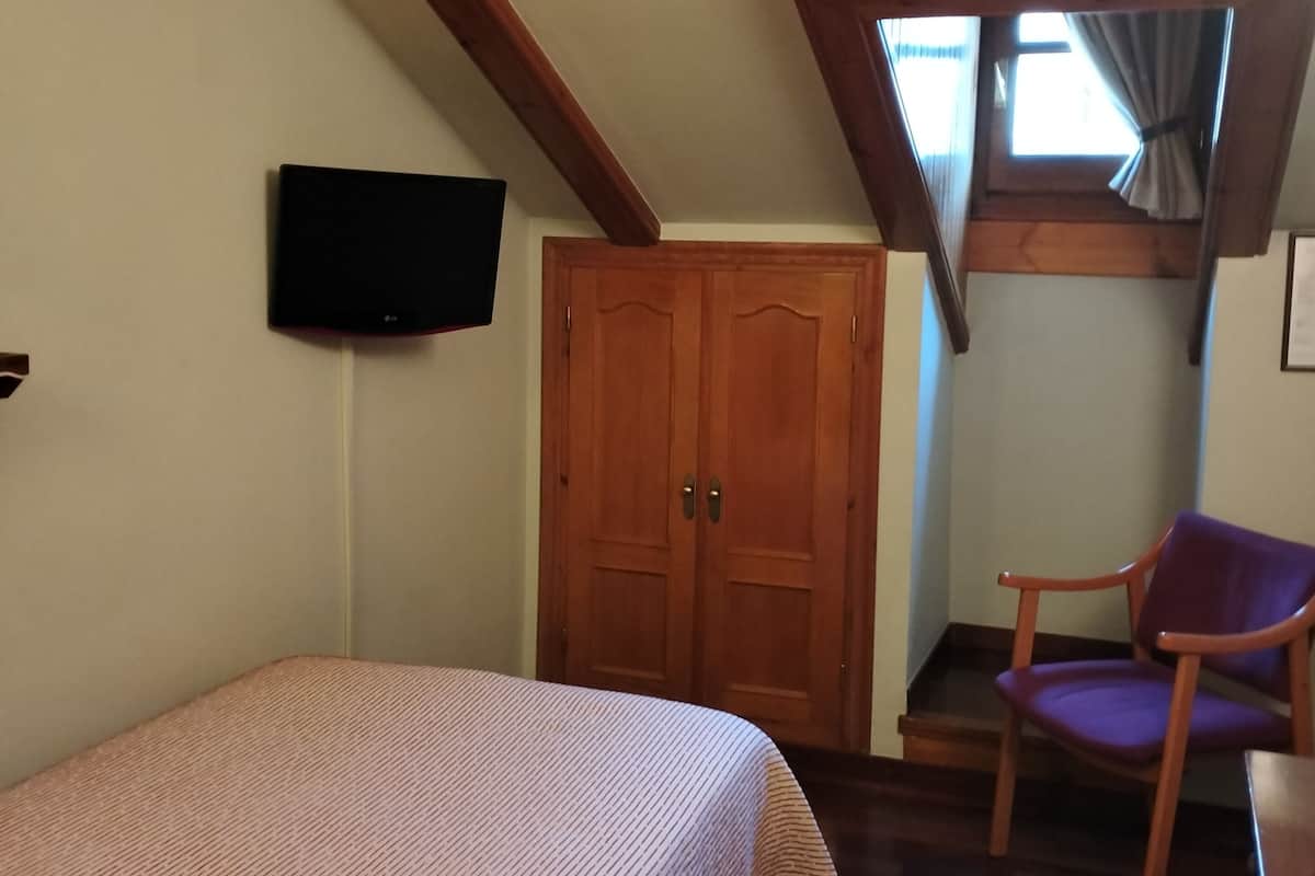 Un dormitorio con cama, una silla, armario y televisor en la pared.