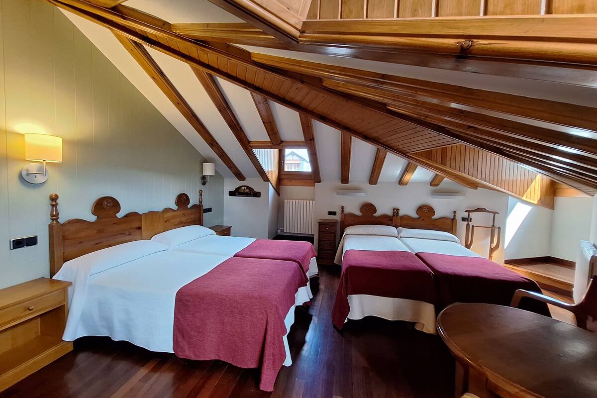 Una habitación con dos camas, vigas de madera, una mesa y una silla.