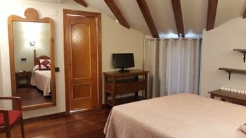 Une chambre avec un plafond en bois, un lit recouvert d’une couvre-lit à motifs, une table de chevet en bois, un téléviseur posé sur une table en bois et un miroir accroché au mur.