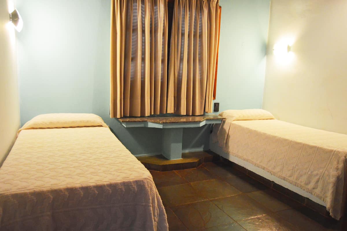 Une chambre avec deux lits simples, un banc et un rideau.