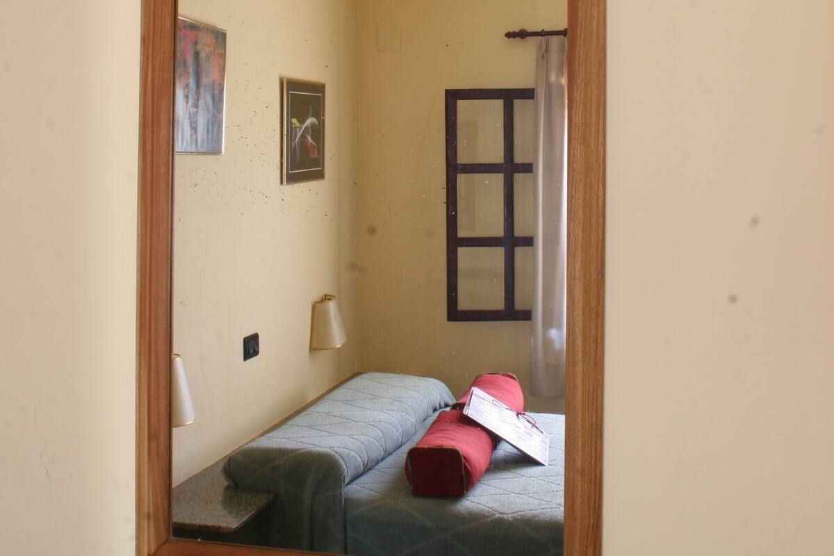 Une pièce avec un lit, un miroir, une lampe et une fenêtre.