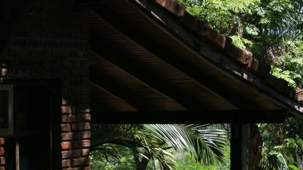 A brick building with a covered porch and a view of a lush garden. - Pirayu Lodge Resort (Puerto Iguazú)