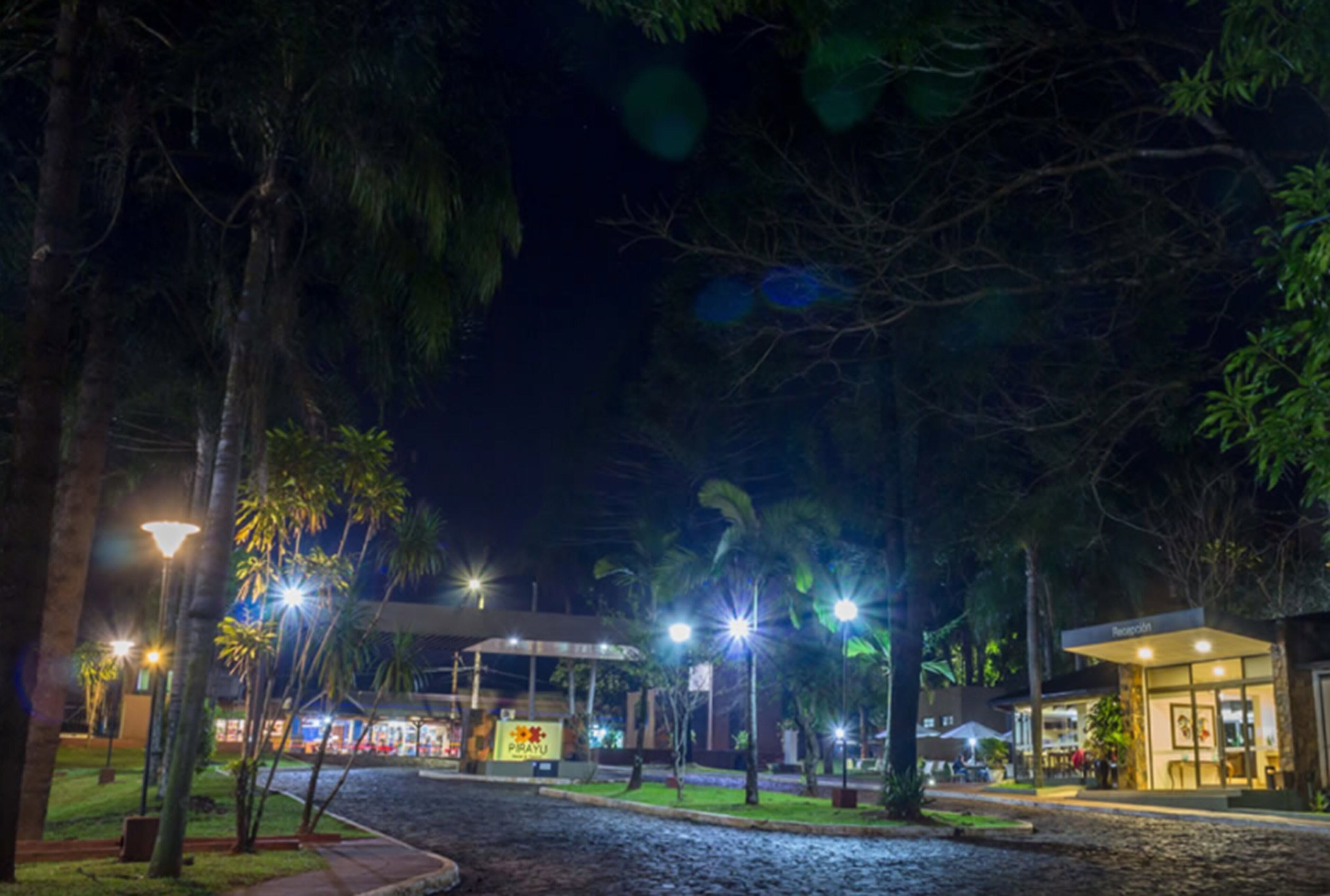 A nighttime view of a hotel with outdoor seating areas, palm trees, and street lamps.