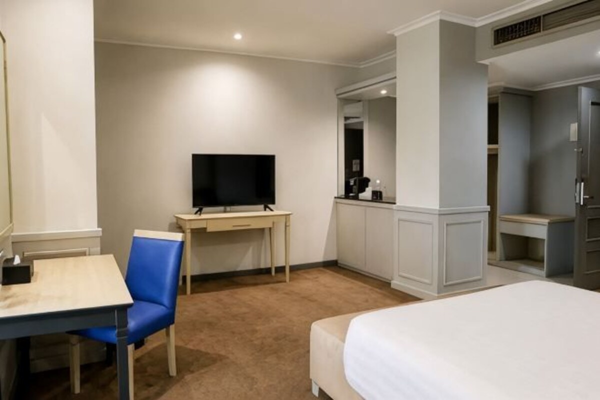 A hotel room with a bed, a desk with a chair, a television, and a wardrobe.