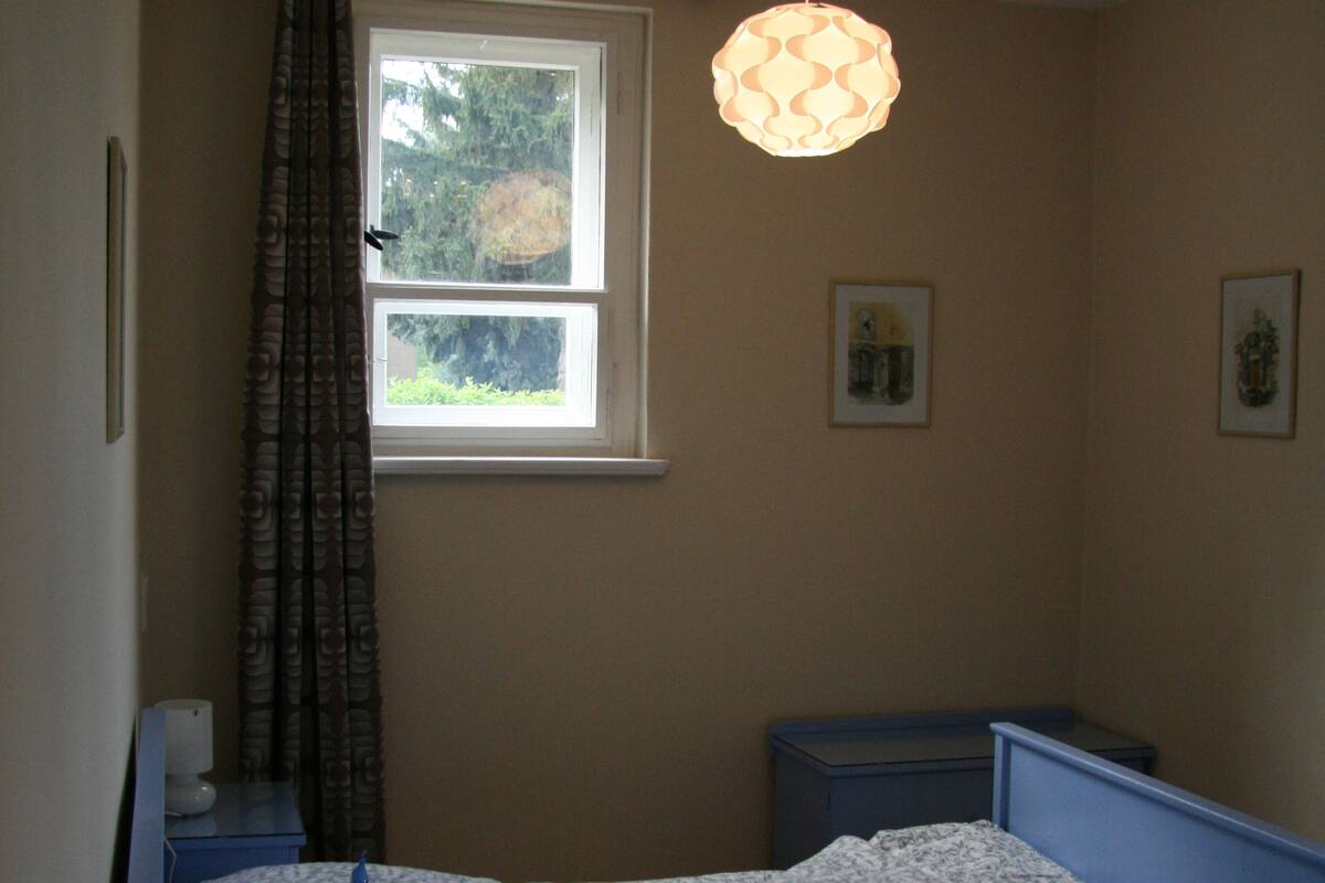Ein Schlafzimmer mit Bett, Fenster, Pendelleuchte und Nachttisch.