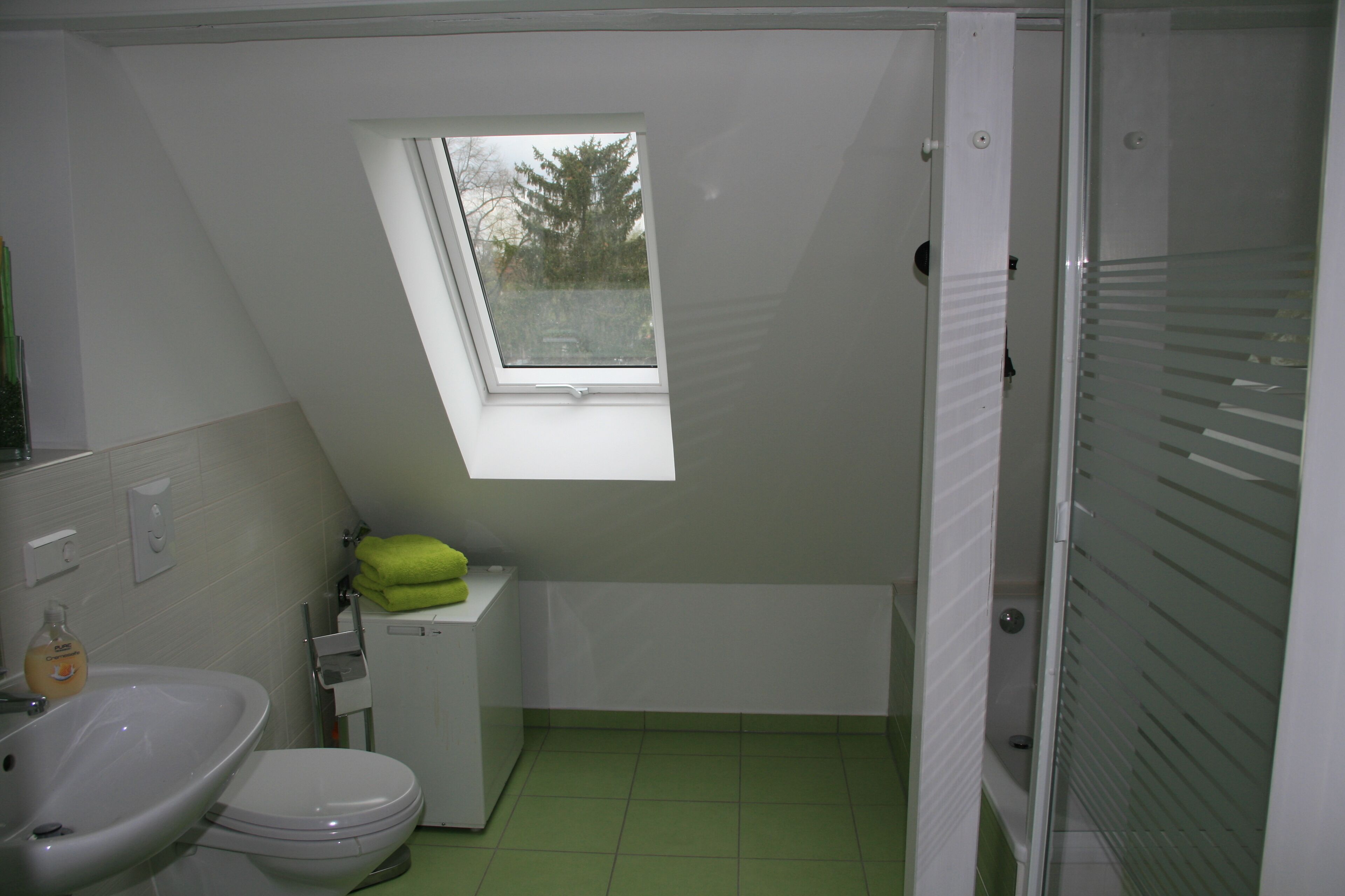 Et lille, kompakt badeværelse med skydelugt, toilet, vask og bruseområde.