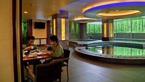 A restaurant with a pool in the center, surrounded by pillars and a TV mounted on the wall. - Gino Feruci Kebonjati (Bandung)