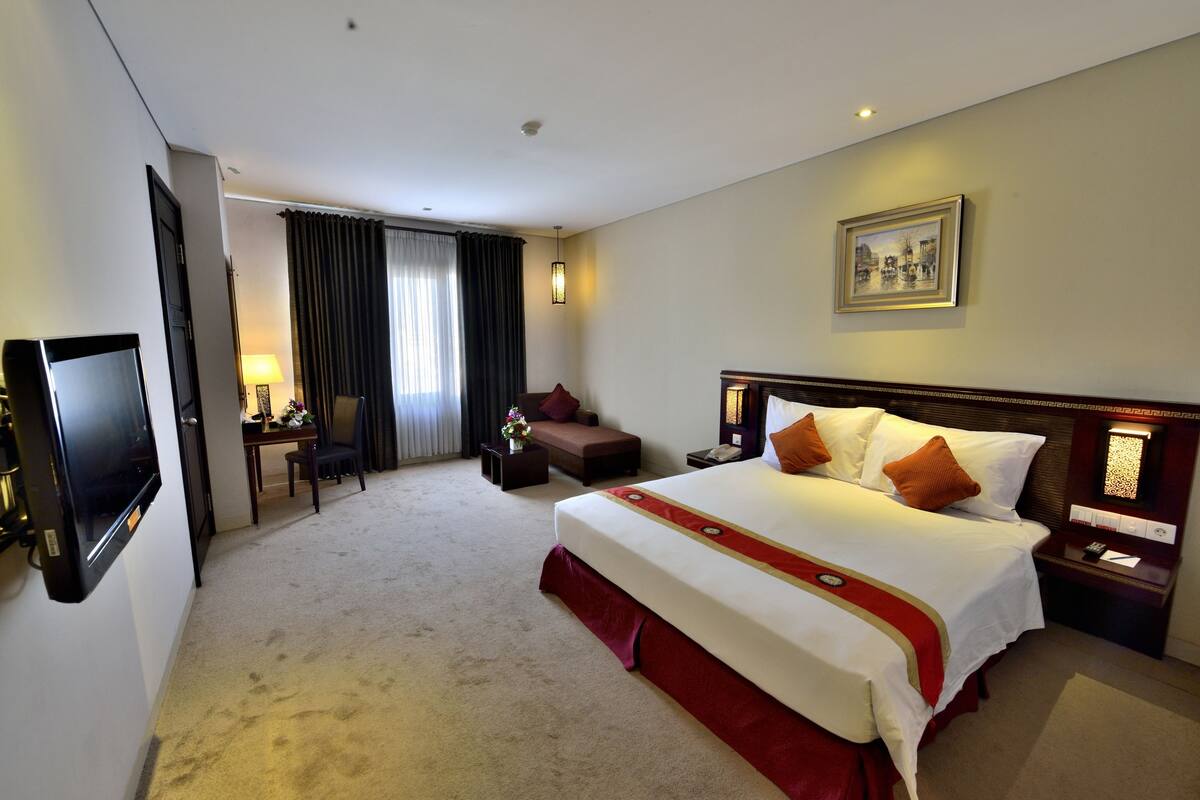 A hotel room with a large bed, a desk with a chair, a TV, and a painting on the wall.