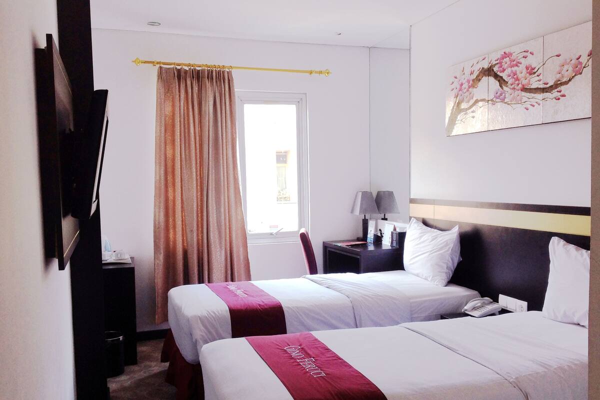 A hotel room with two beds, a desk, a chair, a nightstand, a lamp, and a painting on the wall.