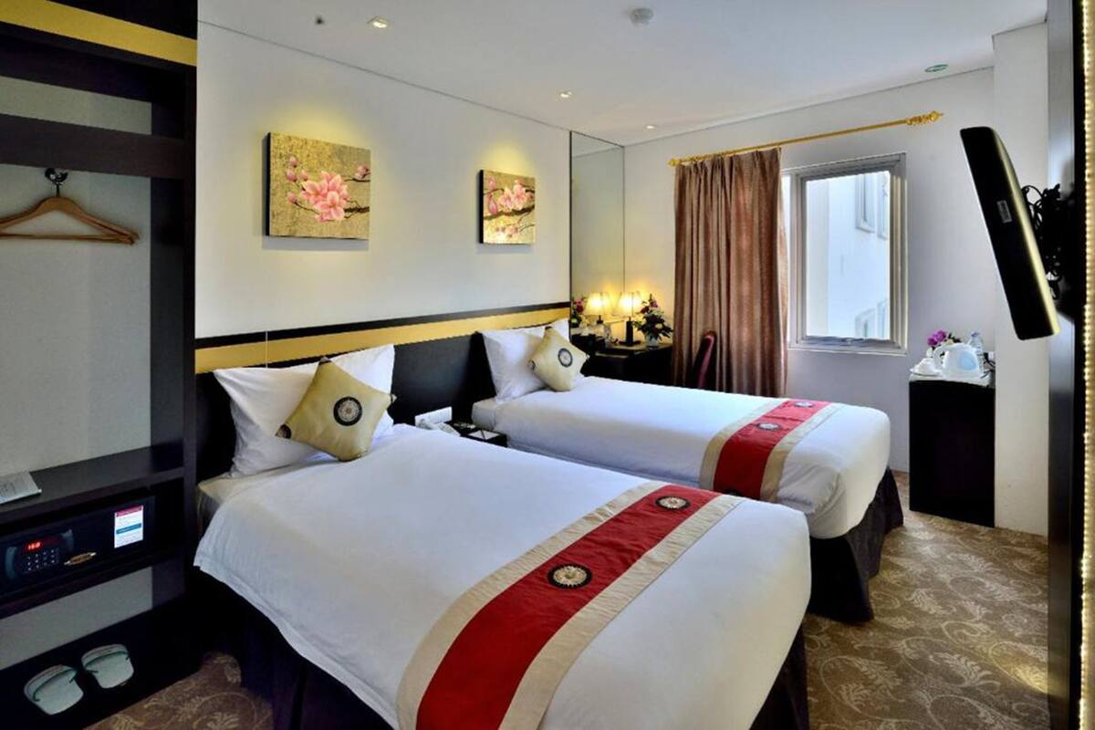 A hotel room with two beds, a bedside table with a lamp, a mirror, and a window with curtains.