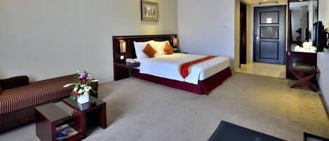 A hotel room with a bed, a sofa, a nightstand, a small table with a vase of flowers, and a door leading to a bathroom.