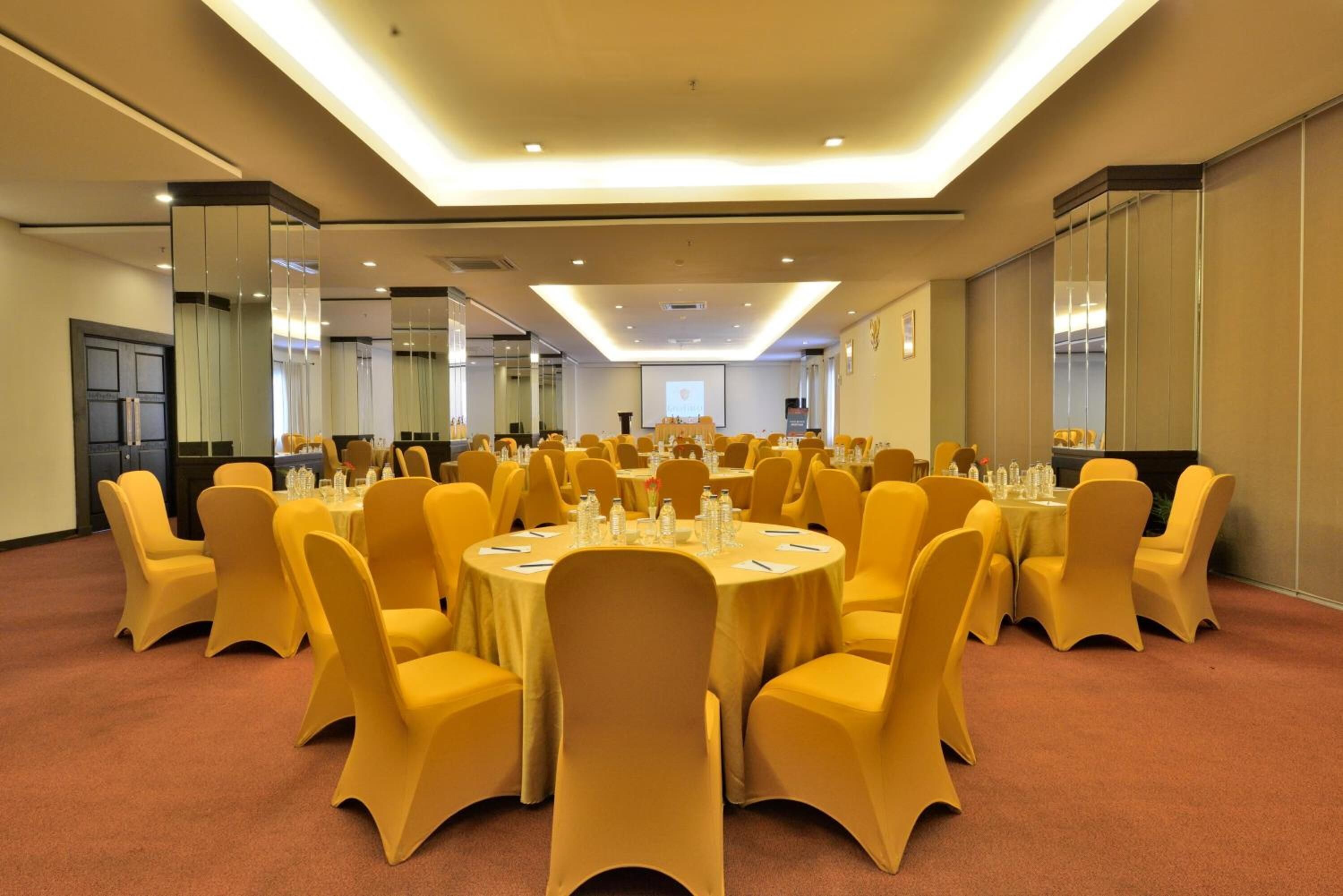 A conference room with multiple round tables and yellow chairs, equipped with water bottles and nameplates.