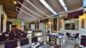 A spacious hotel dining area with multiple tables and chairs, a buffet station, and a high ceiling with skylights. - Gino Feruci Kebonjati (Bandung)
