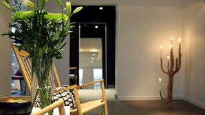 Un interior moderno con una silla de madera, un florero con plantas verdes y un candelabro con velas.
