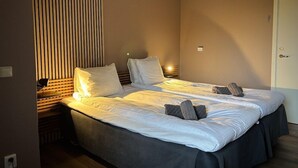 Una cama doble con sábanas blancas, un cabecero de madera y una mesita de noche con lámpara.